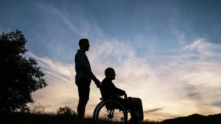 Adult child standing beside father in a wheelchair