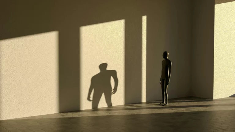 Person facing an enlarged shadow on a wall